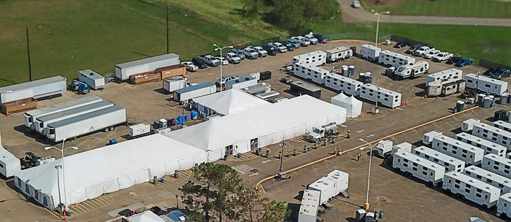 An aerial view of DRG logistics base camp with a large housing tent in a parking lot next to a green field.
