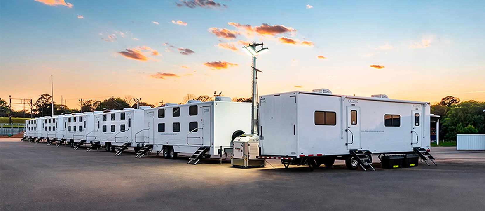 A row of DRG mobile equipment trailers in a parking lot at sunset.