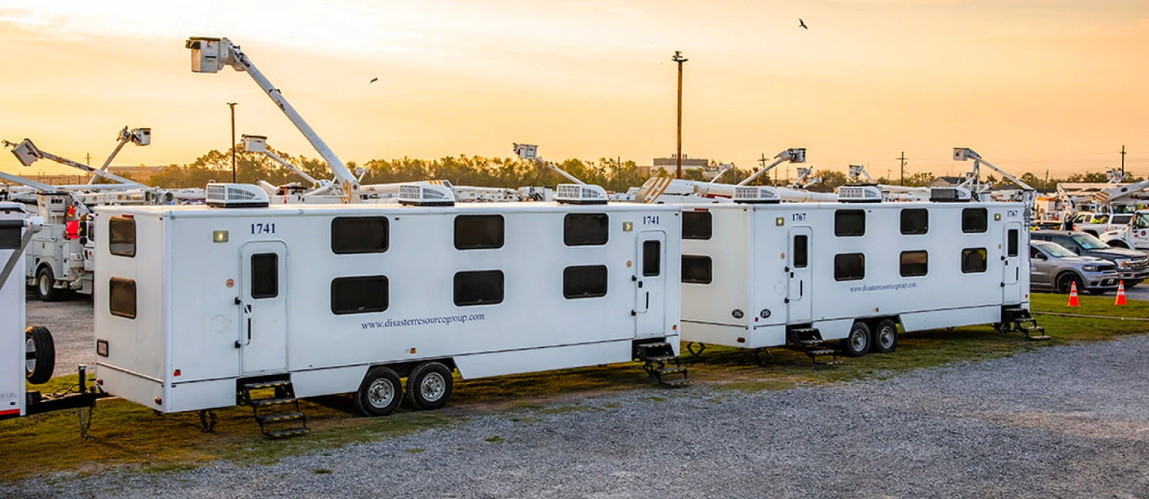 White DRG mobile equipment trailers and utility lifts staged at a logistics base camp.