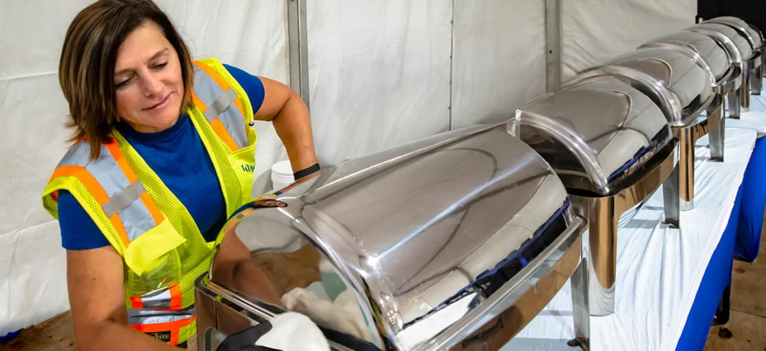 A DRG food service employee sets up warming dishes inside a dining tent.
