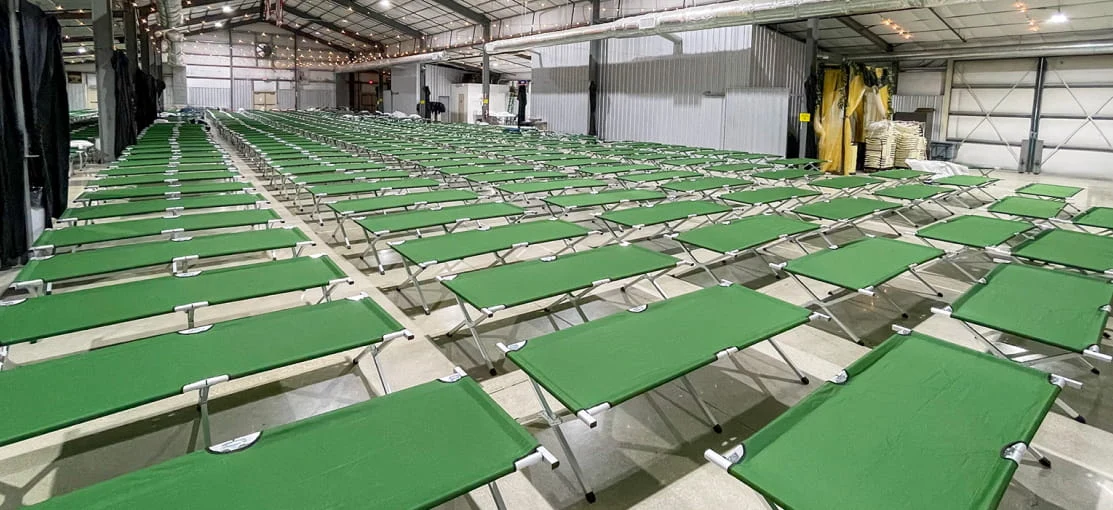Sleeping cots deployed inside a large housing tent.