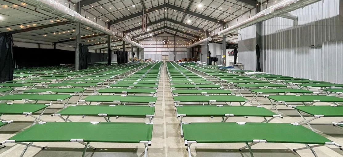 Interior of a large housing tent with sleeping cots deployed throughout.