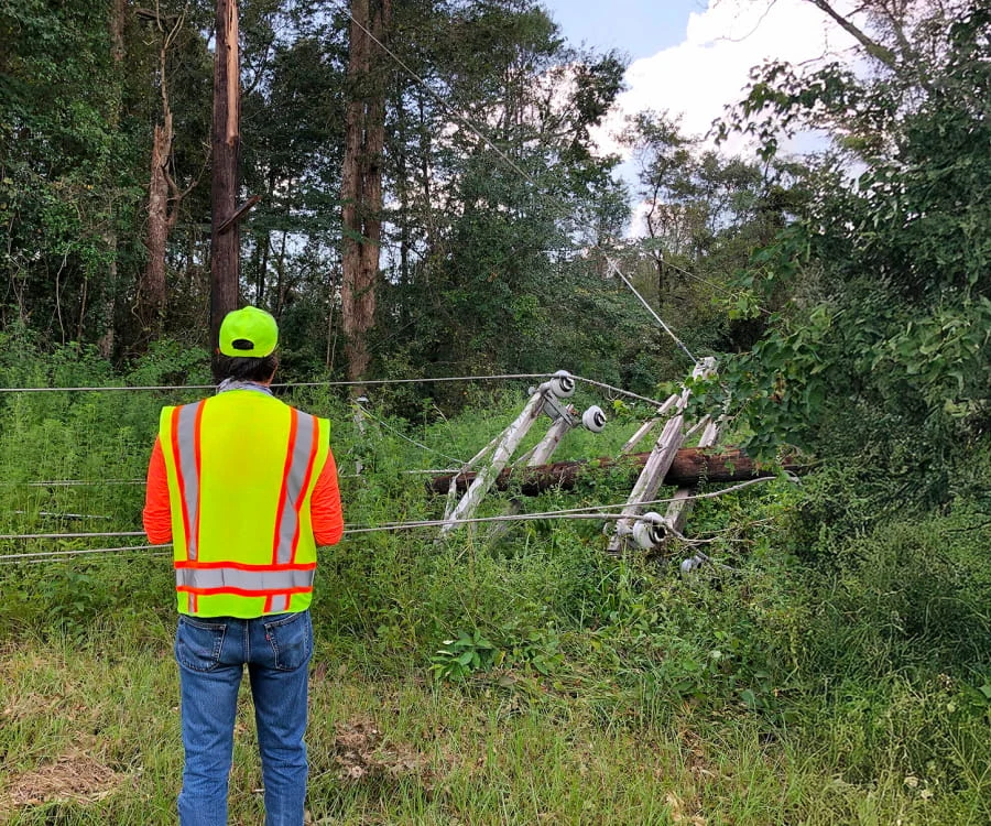 A DRG employee in a yellow and orange vest surveys a downed telephone pole.