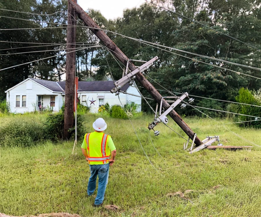 A DRG employee surveys damaged power lines and poles in front of a house.