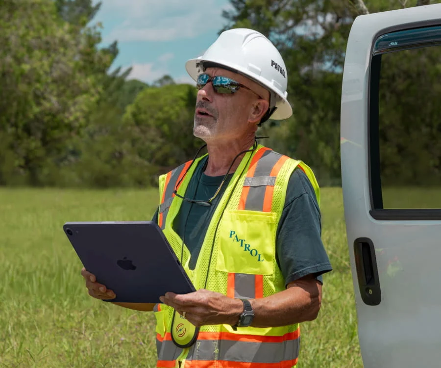 A DRG employee in a yellow vest with a digital tablet in hand surveys storm damage.